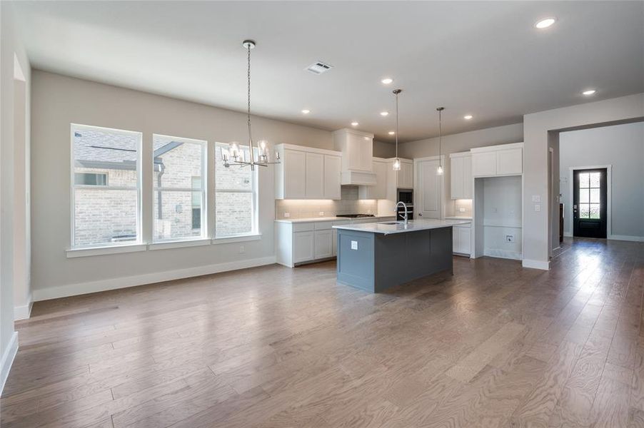 Kitchen with custom exhaust hood, a kitchen island with sink, hardwood / wood-style floors, and pendant lighting