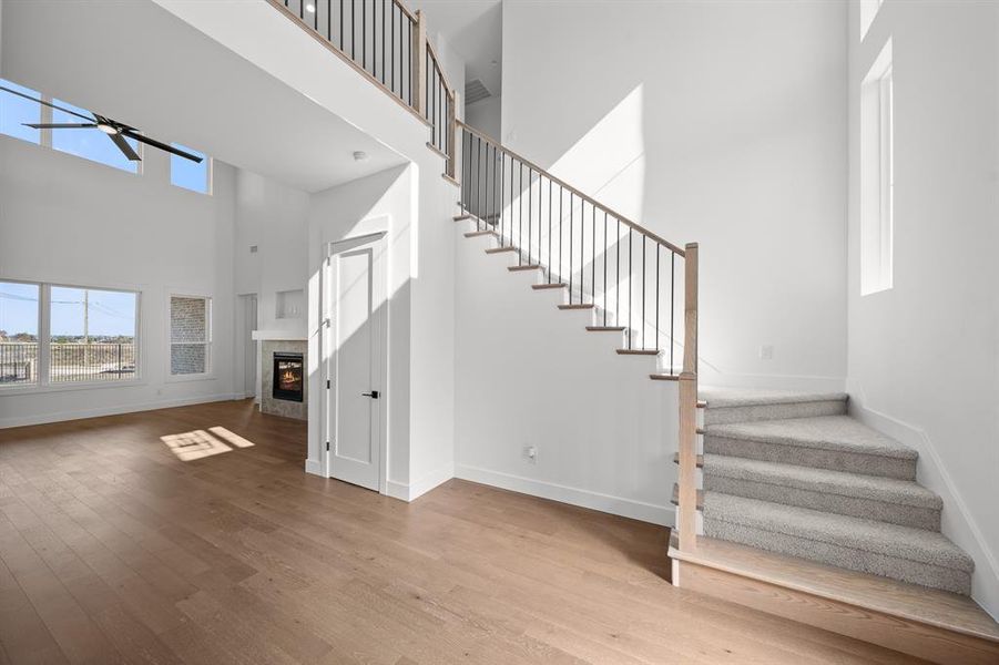 Unfurnished living room featuring stairs, a towering ceiling, a tile fireplace, light wood-style flooring, and a ceiling fan