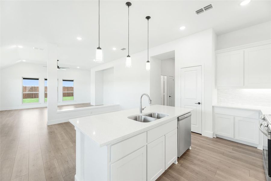 Kitchen with white island, double sink, pendant lights, and open view to living room with wood floors