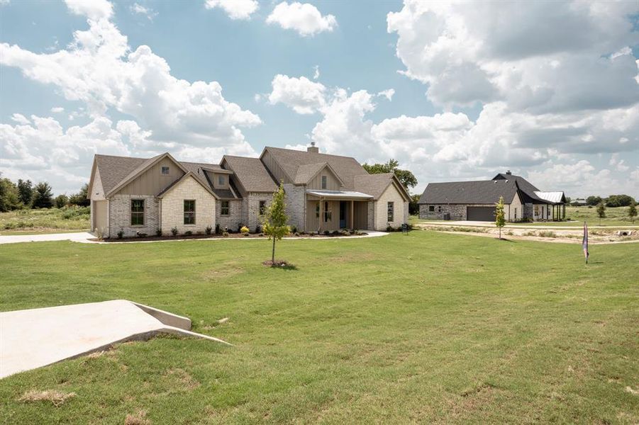 View of front of home featuring board and batten siding, stone siding, a front lawn, and covered porch View of front of home featuring board and batten siding, stone siding, a front lawn, and covered porch