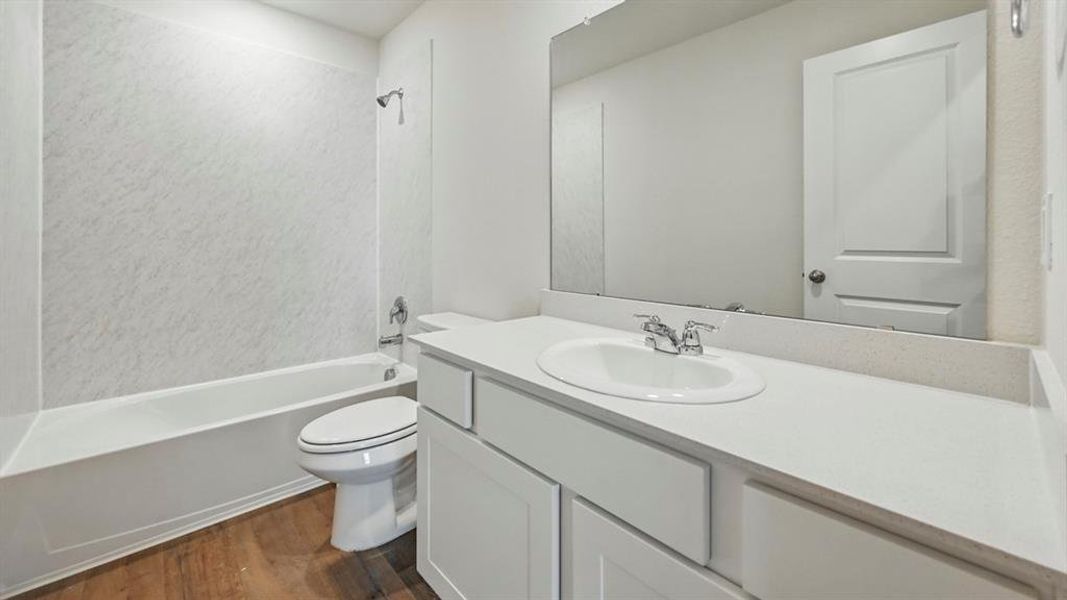 Bathroom featuring a white bathtub with a shower, a toilet, and a vanity with a white countertop and integrated sink
