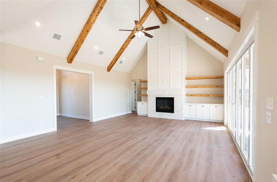 Unfurnished living room featuring high vaulted ceiling, ceiling fan, light wood-type flooring, beamed ceiling, and a fireplace