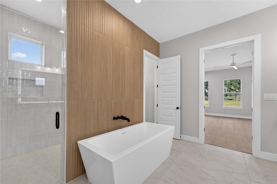 A modern freestanding tub sits against a textured wood-look wall panel beneath recessed lighting.