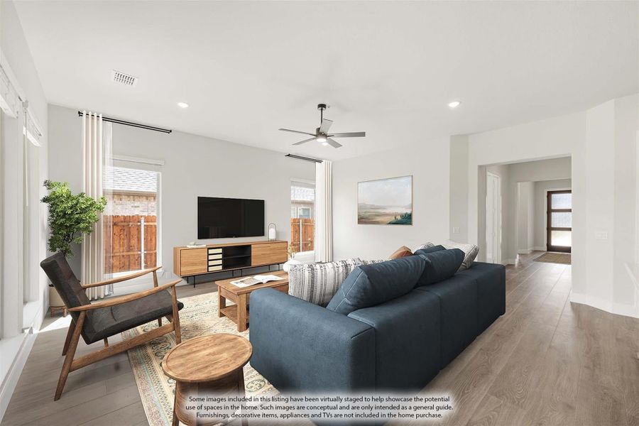 Living room with blue sofa, wood floors, ceiling fan, and TV on a wood media console