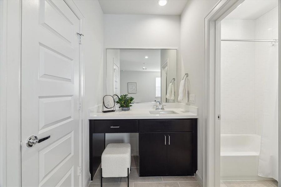 This modern first-floor ensuite bathroom offers a sleek design with a spacious vanity and plenty of counter space. The door on the left leads to a walk-in closet, while the galley layout provides easy access to the shower/tub combination located in a separate water closet for added privacy. Clean lines, bright lighting, and neutral tones create a functional and welcoming space, perfect for guests or daily use.