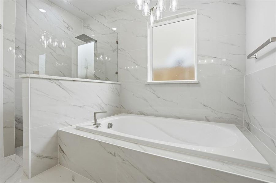 Integrated soaking tub with deck-mounted faucet set, surrounded by large format tile with marble-effect veining