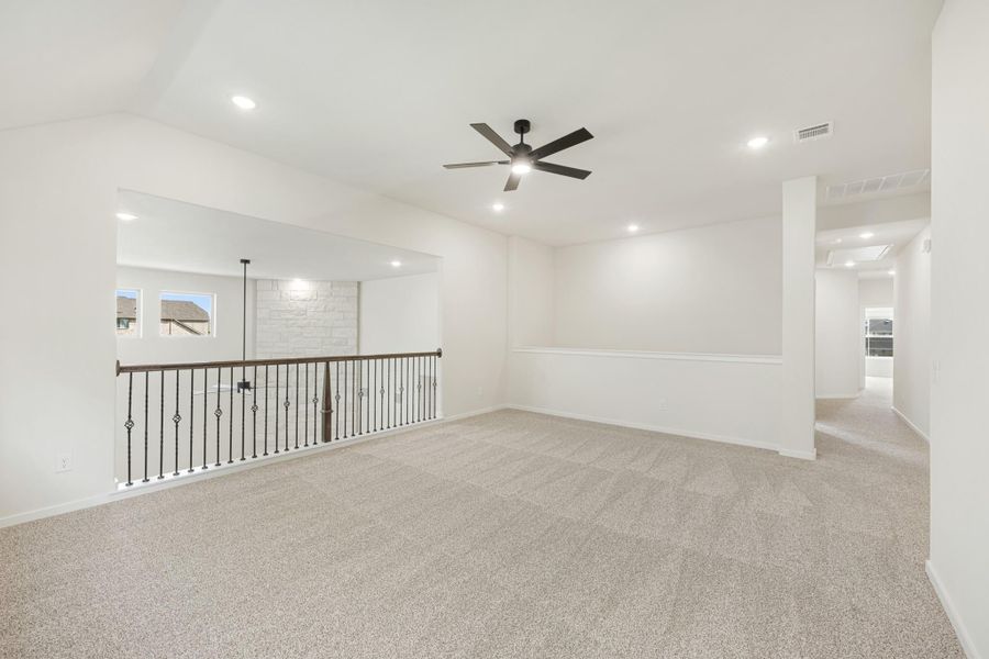 Upstairs bonus room with carpet, ceiling fan, and iron stair railing overlooking lower level