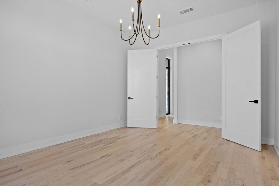 Spare room with baseboards, visible vents, light wood finished floors, and a chandelier