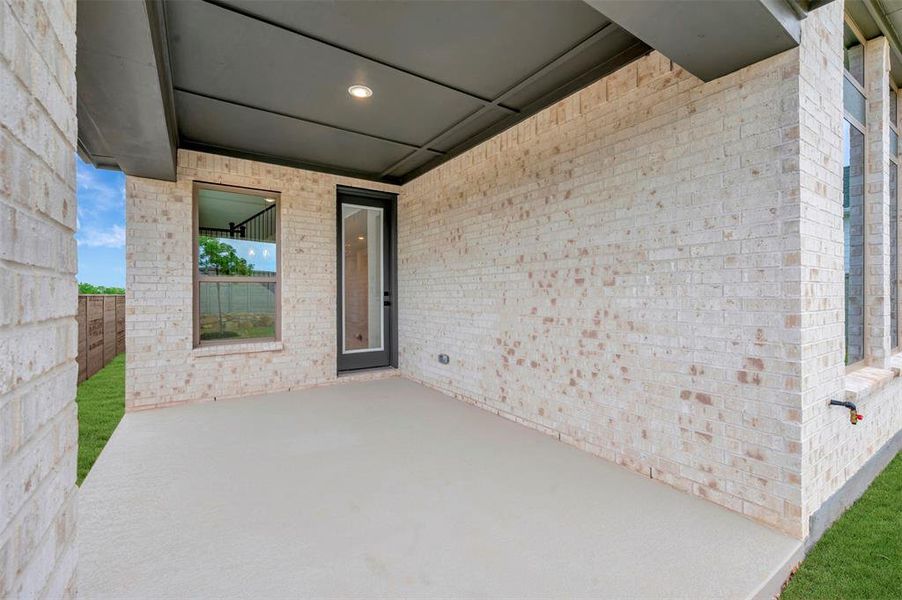 The property features a covered patio with a smooth concrete surface, an exterior brick wall, and a large window