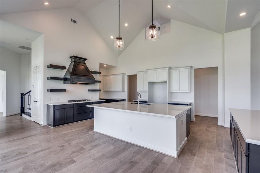 Kitchen with an island with sink, high vaulted ceiling, light wood-type flooring, and custom exhaust hood