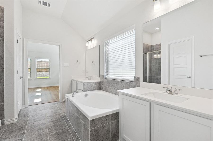 Bathroom with tiled tub, oversized vanity, tile floors, and lofted ceiling