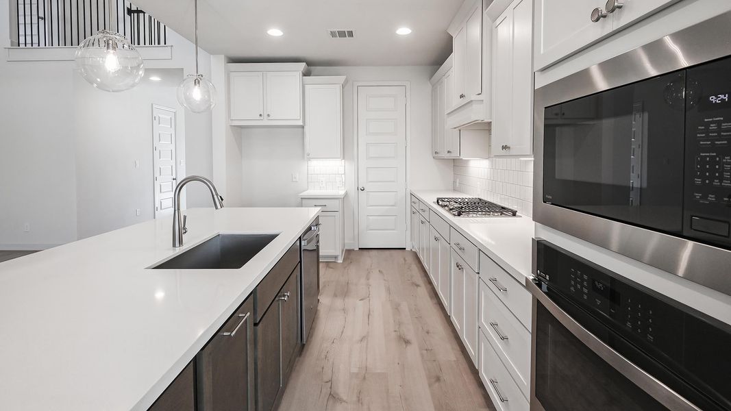 Kitchen featuring appliances with stainless steel finishes, decorative light fixtures, white cabinetry, light wood-type flooring, and decorative backsplash Kitchen featuring appliances with stainless steel finishes, decorative light fixtures, white cabinetry, light wood-type flooring, and decorative backsplash