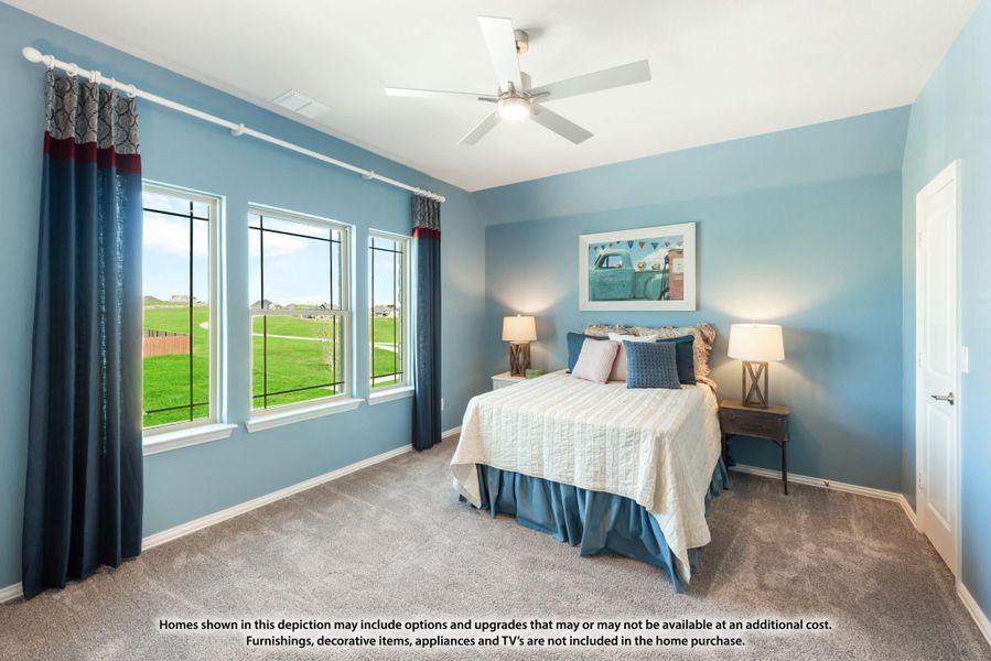Bedroom with blue walls, ceiling fan, carpet flooring, and three windows with curtains overlooking a green lawn