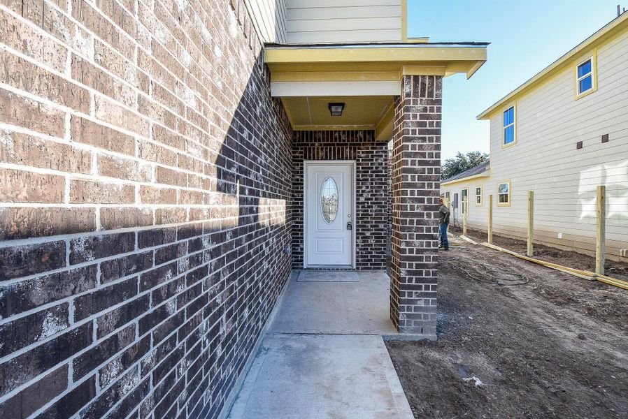 A narrow alley leading to a house entrance with a white door, flanked by brick walls, in a newly constructed residential area.