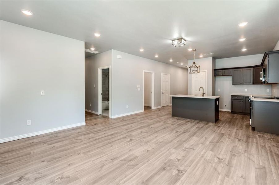 Kitchen featuring light hardwood / wood-style floors, sink, hanging light fixtures, and a kitchen island with sink