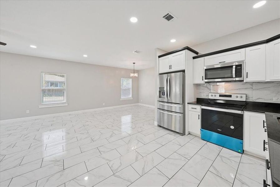 Kitchen with appliances with stainless steel finishes, backsplash, recessed lighting, light marble finish flooring, and white cabinets