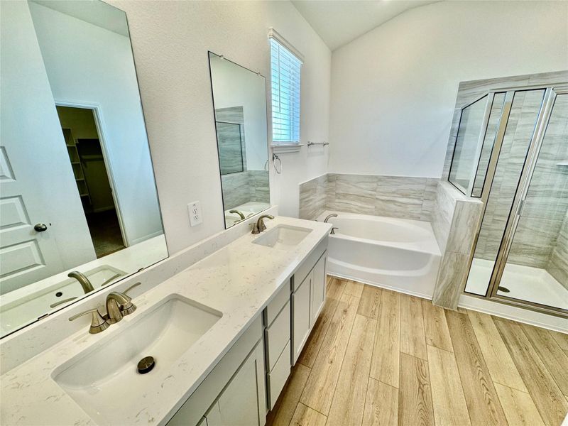 Bathroom featuring a stall shower, a bath, light wood finished floors, double vanity, and vaulted ceiling Bathroom featuring a stall shower, a bath, light wood finished floors, double vanity, and vaulted ceiling
