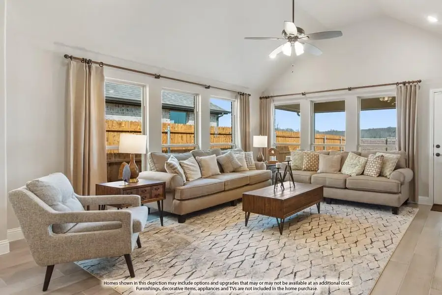 Living room with vaulted ceiling, ceiling fan, large windows, and neutral-toned sofas on a patterned area rug