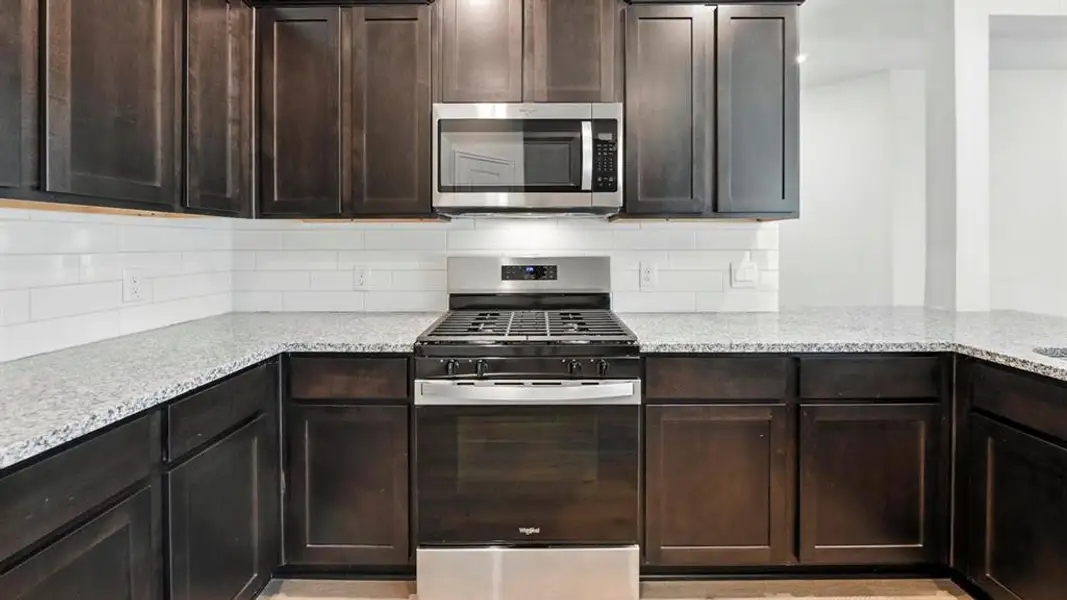 Kitchen with stainless steel appliances, tasteful backsplash, light stone counters, and dark brown cabinets