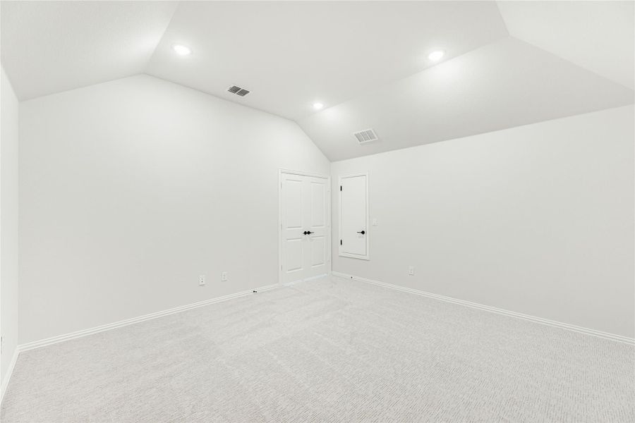 Empty bedroom with vaulted ceiling, recessed lighting, carpet flooring, and two white doors