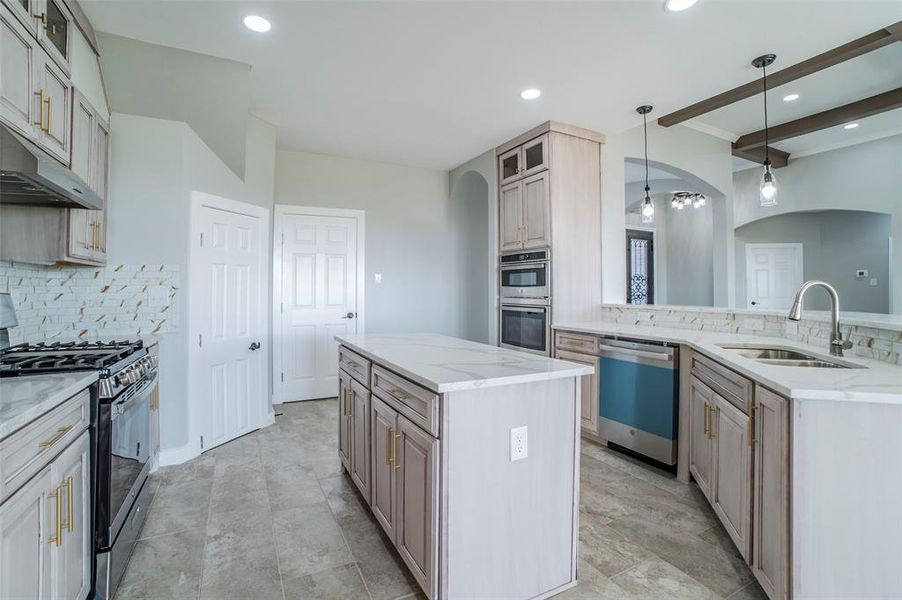 Kitchen featuring glass insert cabinets, a kitchen island, stainless steel appliances, tasteful backsplash, and light stone countertops Kitchen featuring glass insert cabinets, a kitchen island, stainless steel appliances, tasteful backsplash, and light stone countertops