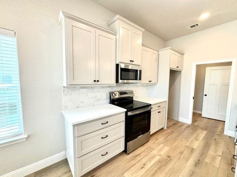 Kitchen with decorative backsplash, white cabinetry, light hardwood / wood-style flooring, and appliances with stainless steel finishes