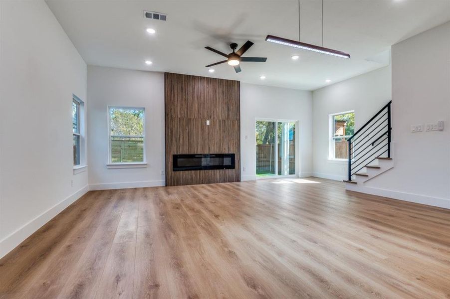 Unfurnished living room featuring ceiling fan, a large fireplace, stairway, recessed lighting, and light wood-type flooring