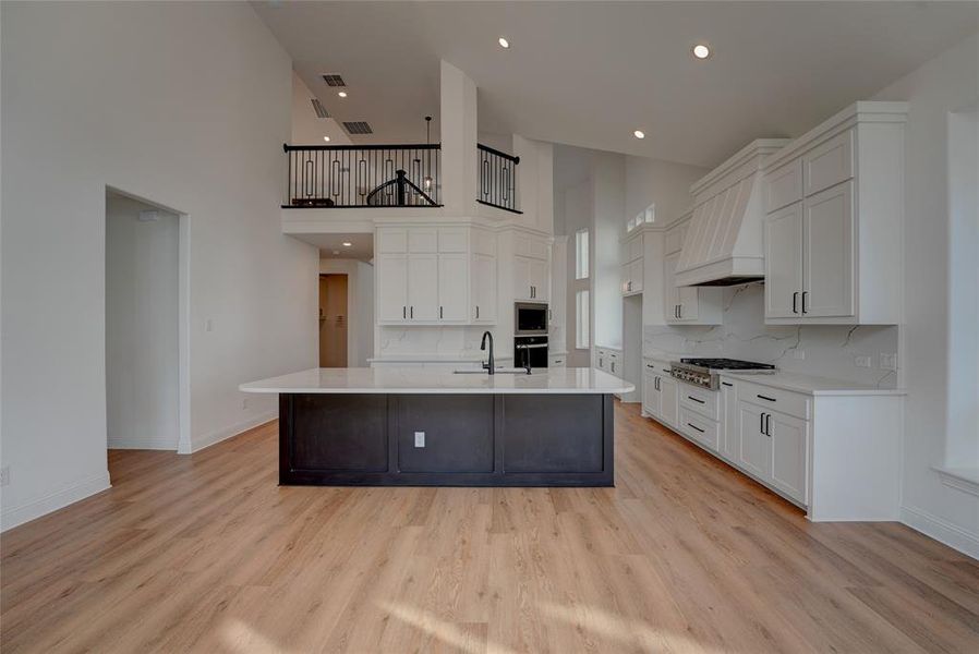 Kitchen with white cabinets, custom range hood, stainless steel appliances, and light countertops