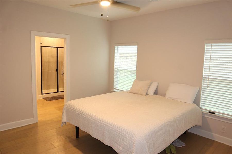 Bedroom with light wood finished floors, a ceiling fan, and ensuite bathroom Bedroom with light wood finished floors, a ceiling fan, and ensuite bathroom