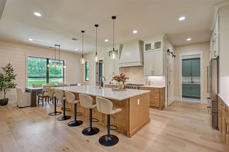 The heart of the home — quartz Taj Mahal countertops, an oversized island built for gathering, and a chef's dream lineup: a 48-inch 6-burner range with double convection ovens and griddle, commercial grade vent hood, built-in drawer microwave, hidden trash drawer, pot and pan drawers, soft-close cabinets and drawers throughout, elevated tile backsplash, and crown molding to the ceiling. This is where your next dinner party — and a thousand memories after — get made. The heart of the home — quartz Taj Mahal countertops, an oversized island built for gathering, and a chef's dream lineup: a 48-inch 6-burner range with double convection ovens and griddle, commercial grade vent hood, built-in drawer microwave, hidden trash drawer, pot and pan drawers, soft-close cabinets and drawers throughout, elevated tile backsplash, and crown molding to the ceiling. This is where your next dinner party — and a thousand memories after — get made.