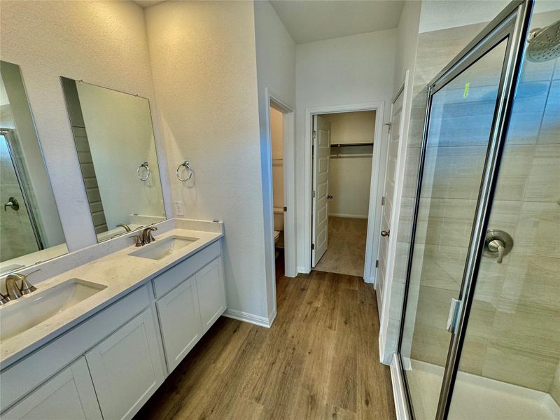 Bathroom featuring a stall shower, a walk in closet, double vanity, dark wood finished floors, and a textured wall