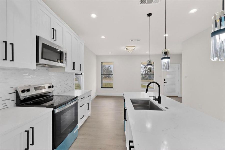 Kitchen with stainless steel appliances, white cabinetry, pendant lighting, and light stone counters Kitchen with stainless steel appliances, white cabinetry, pendant lighting, and light stone counters
