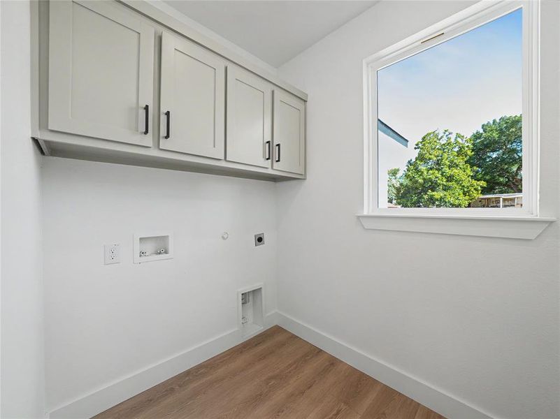 Laundry area featuring wood-finish flooring, white walls, and a window with a white frame Laundry area featuring wood-finish flooring, white walls, and a window with a white frame