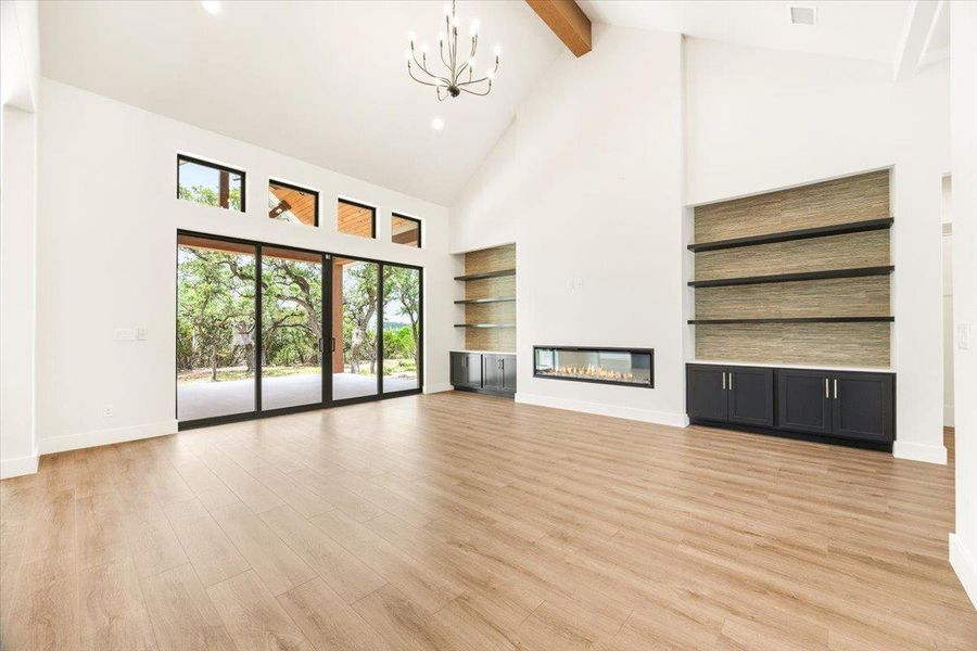 A spacious great room showcases high vaulted ceilings, elegant flooring, and a modern fireplace with a natural outdoor view.