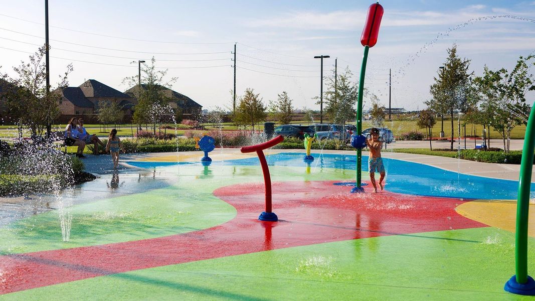 This photo showcases a vibrant community splash pad with colorful play features and water jets, perfect for family fun in a suburban neighborhood setting.
