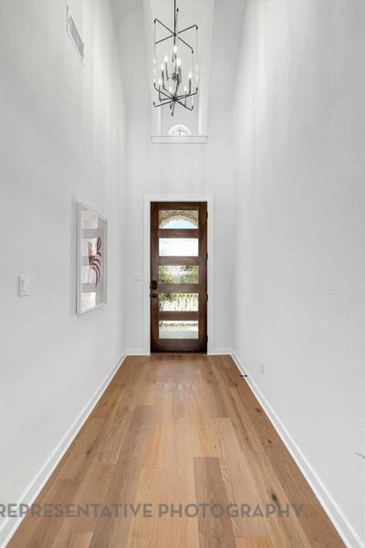 Entrance foyer featuring a chandelier, light wood finished floors, and a towering ceiling Entrance foyer featuring a chandelier, light wood finished floors, and a towering ceiling