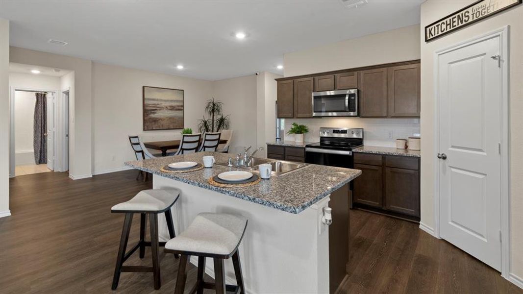 Kitchen featuring a breakfast bar, stainless steel appliances, dark wood finish cabinetry, dark wood finished floors, and an island with sink