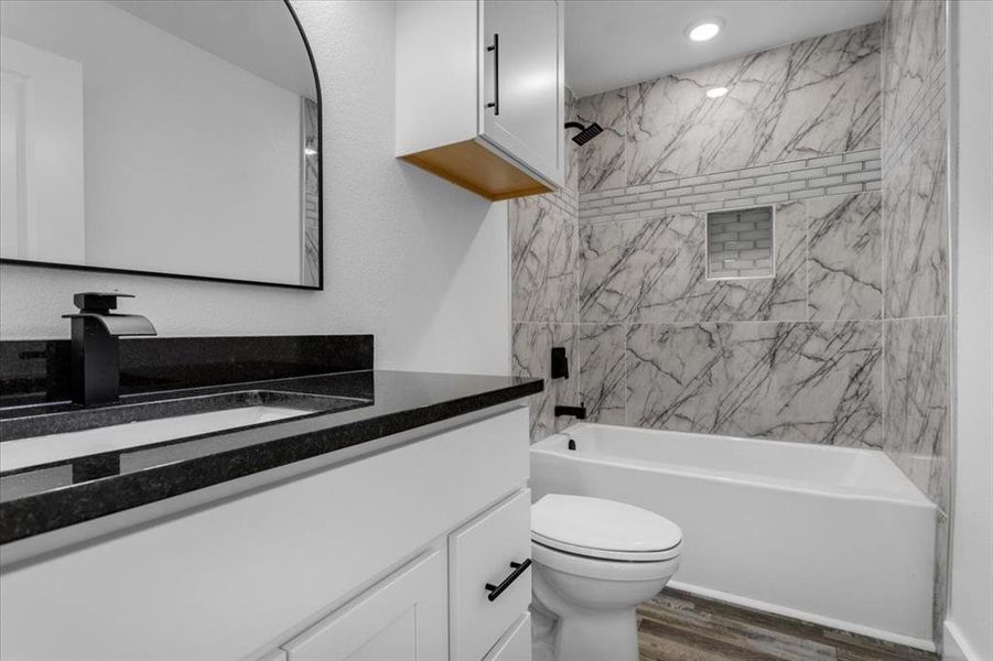 Full bathroom with tiled shower / bath, vanity, hardwood / wood-style floors, and toilet