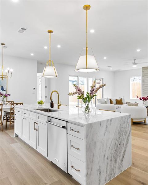 Kitchen with hanging light fixtures, an island with sink, sink, and stainless steel dishwasher