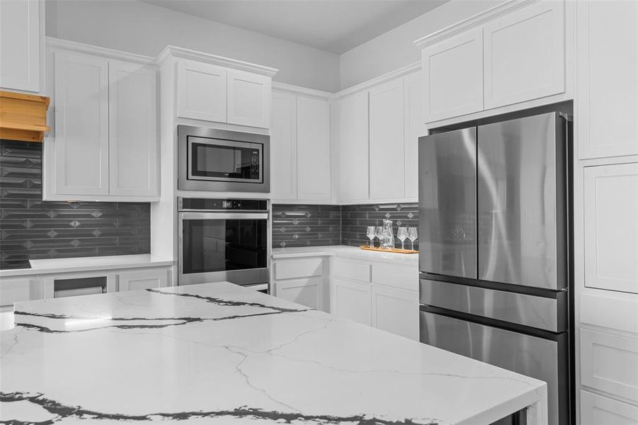 Kitchen with decorative backsplash, light stone countertops, white cabinetry, and stainless steel appliances