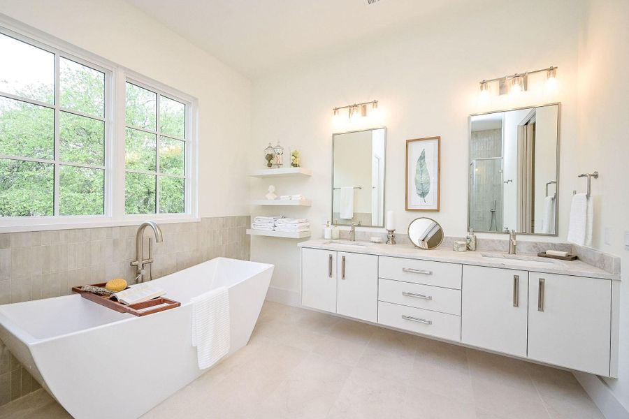 This primary bathroom features a modern design with a spacious freestanding tub, dual sinks with mirrored vanities, and ample natural light from large windows. Neutral tones and sleek fixtures enhance its elegant and calming atmosphere.