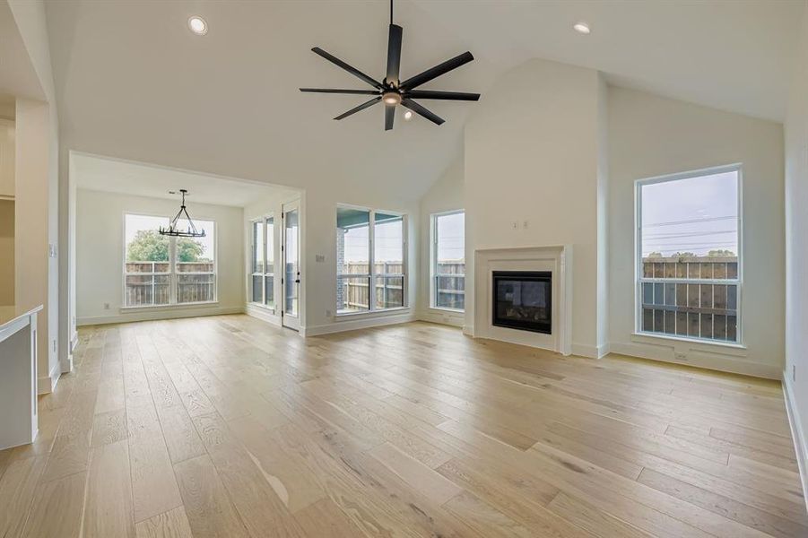 Unfurnished living room featuring high vaulted ceiling, light wood-style floors, a glass covered fireplace, recessed lighting, and a ceiling fan Unfurnished living room featuring high vaulted ceiling, light wood-style floors, a glass covered fireplace, recessed lighting, and a ceiling fan