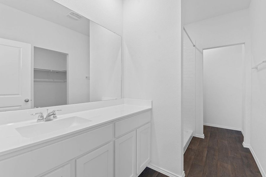 Full bath with visible vents, vanity, wood finished floors, baseboards, and walk in shower