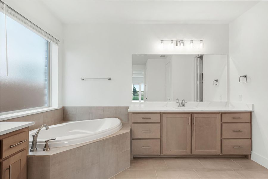 Master bathroom with corner soaking tub, wood vanity, white countertop, and large mirror with light bar.