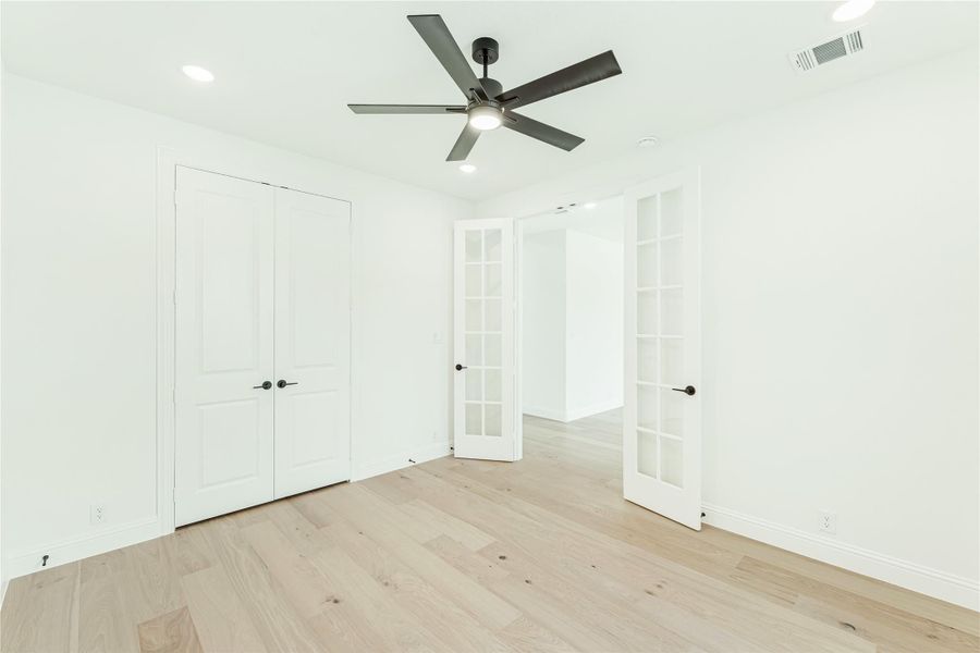 Empty bedroom with light hardwood floors, ceiling fan, closet, and French doors leading to adjoining room