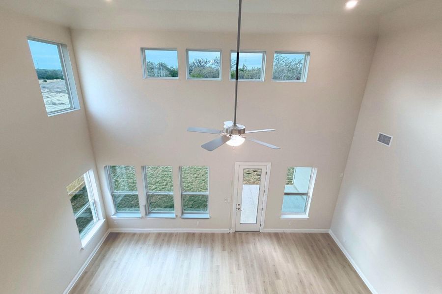 Unfurnished living room featuring plenty of natural light, light wood-style floors, a towering ceiling, and ceiling fan