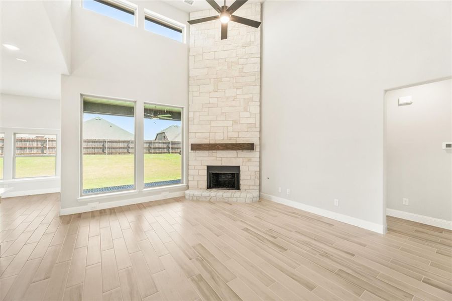Open living room with two-story stone fireplace, light wood floors, and ceiling fan Open living room with two-story stone fireplace, light wood floors, and ceiling fan
