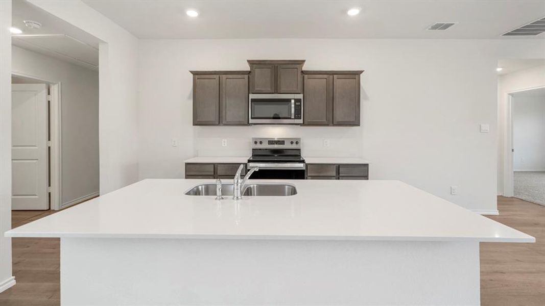 Kitchen featuring a large island with a double basin sink, stainless steel faucet, and white countertop