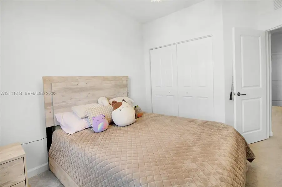Neutral-toned room featuring light-colored wall-to-wall carpeting, high-reaching ceilings, and a built-in double-door closet with paneled detailing Neutral-toned room featuring light-colored wall-to-wall carpeting, high-reaching ceilings, and a built-in double-door closet with paneled detailing