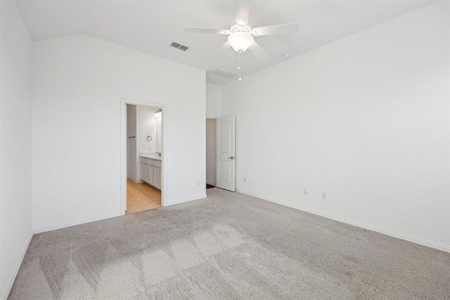 Unfurnished Primary Bedroom with vaulted ceiling, ceiling fan, ensuite bathroom, and light colored carpet